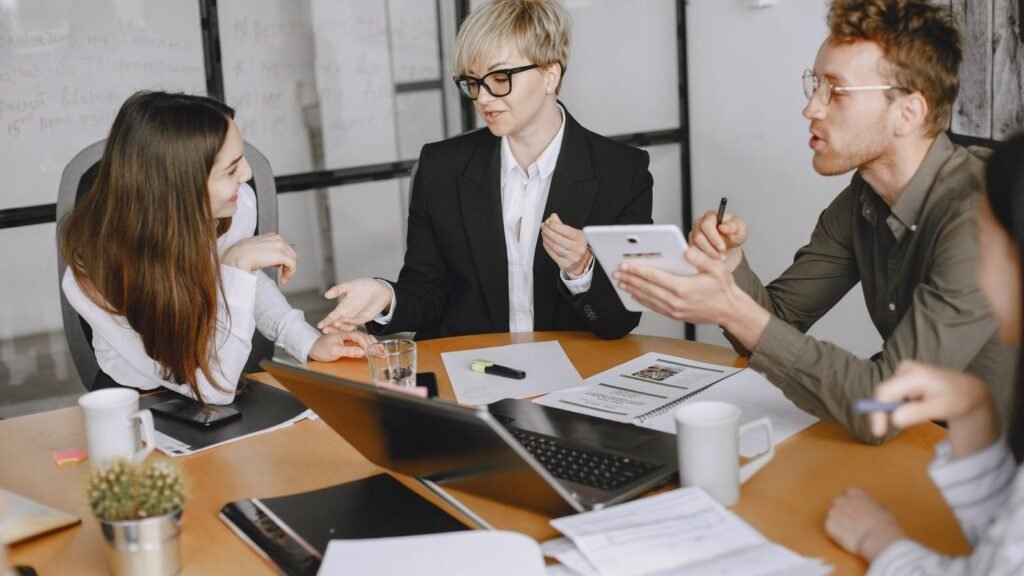 Equipo de trabajo reunido alrededor de una mesa con una notebook y una tableta, conversando sobre tecnología en la empresa