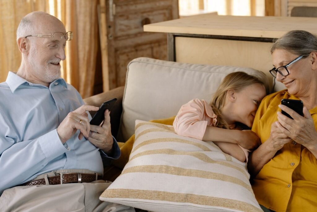 Abuelos con sus celulares y una nieta sonriendo en el sillón de una casa
